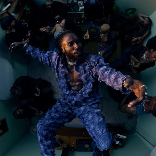 Man in a blue textured outfit surrounded by people in a room with a blue wall.